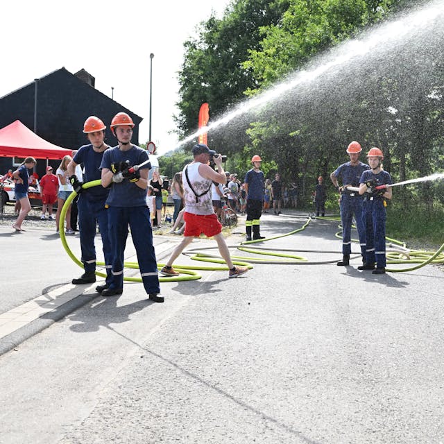 Mehrere junge Feuerwehrleute schießen Wasser aus zwei Schläuchen.