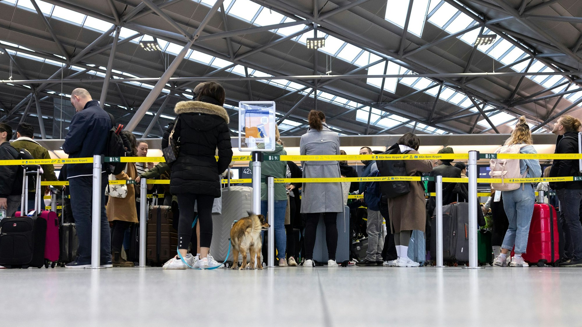 Reisende am Flughafen Köln/Bonn stehen in der Abflughalle an den Check-In Schaltern.
