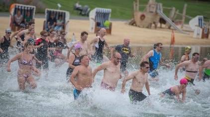 Menschen in Badekleidung laufen für einen Triathlon in den Zülpicher Wassersportsee.
