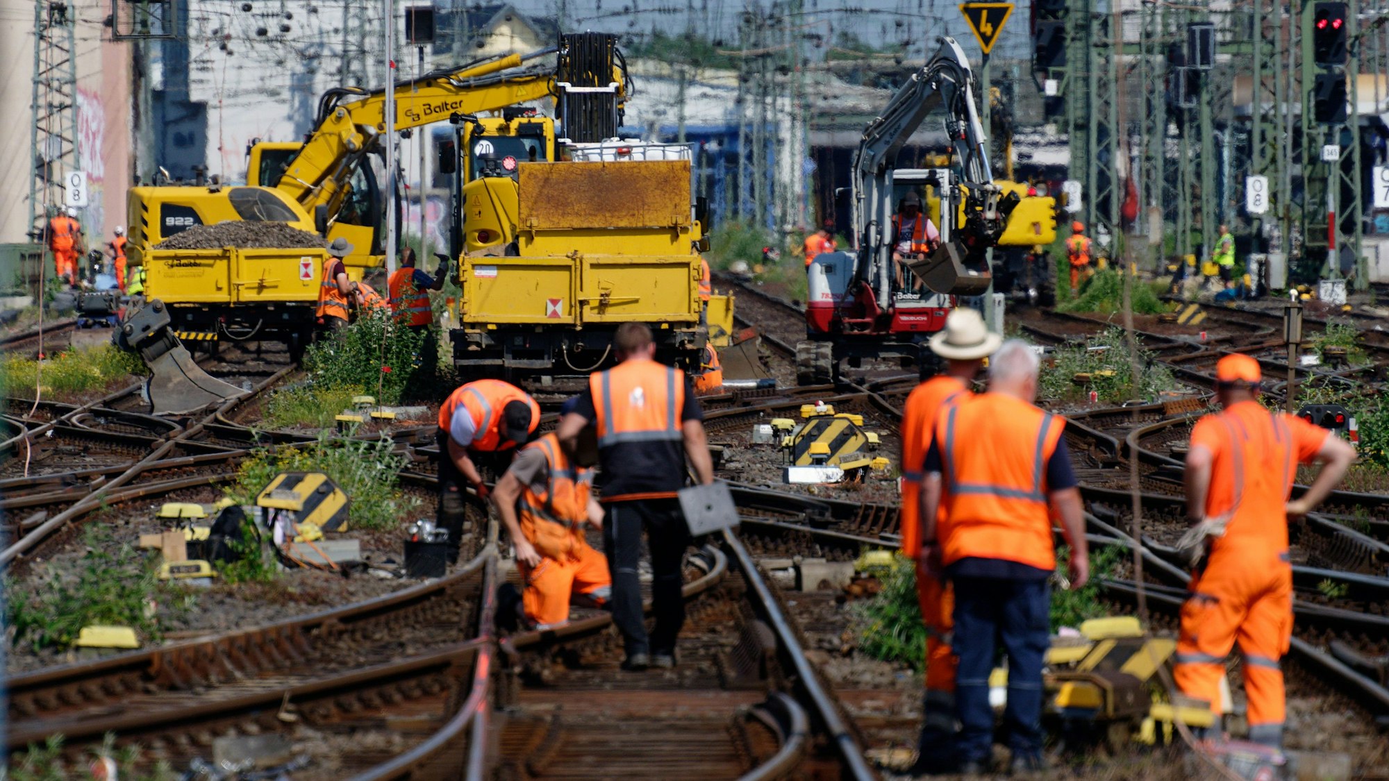 Mitarbeiter der Deutschen Bahn arbeiten an einem Gleis, Kollegen stehen daneben. Auf mehreren Gleisen stehen Maschinen.