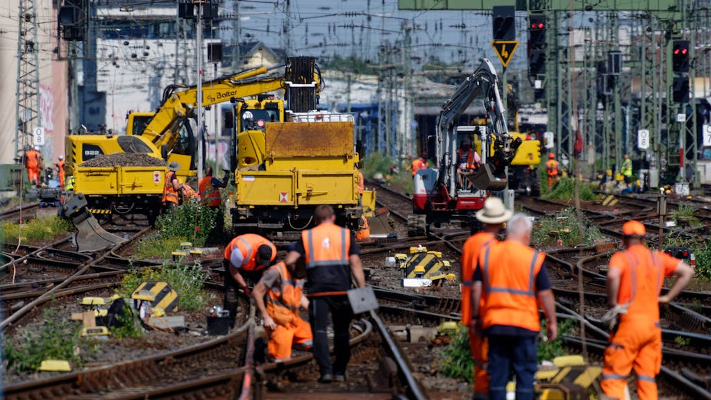 Mitarbeiter der Deutschen Bahn arbeiten an einem Gleis, Kollegen stehen daneben. Auf mehreren Gleisen stehen Maschinen.&nbsp;