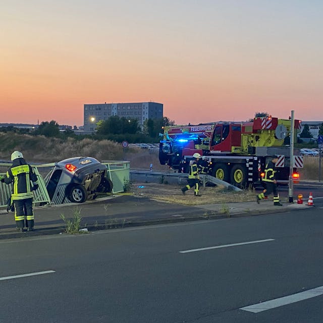 Ein Auto hängt an der Brüstung der Brücke der Merianstraße in Köln-Merkenich. Der Fahrer blieb bei dem Unfall am Freitagabend unverletzt.