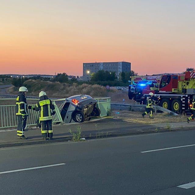 Ein Auto hängt an der Brüstung der Brücke der Merianstraße in Köln-Merkenich. Der Fahrer blieb bei dem Unfall am Freitagabend unverletzt.