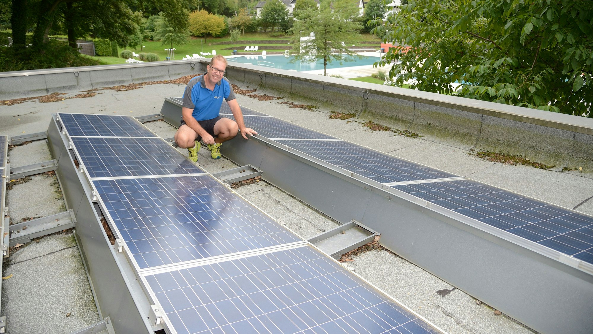 Ein Mann hockt zwischen Photovoltaik-Panelen auf dem Dach der Umkleiden des Hoffnungsthaler Freibads.