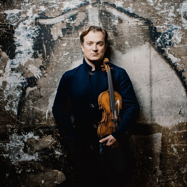 Renaud Capuçon steht vor einer Wand und hält eine Violine in der Hand.