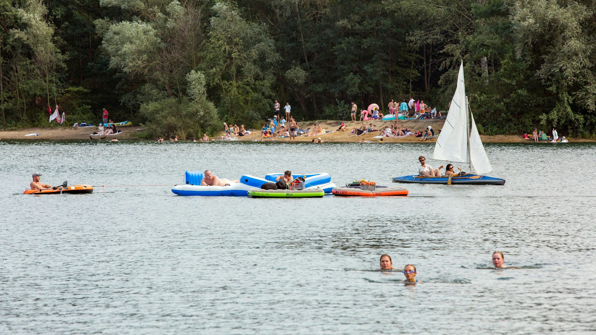 Schlauchboote und ein Segelboot auf einem See, im Vordergrund drei Schwimmerinnen