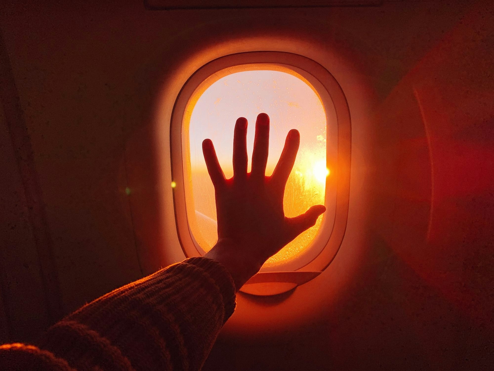 Eine Hand berührt ein Fenster im Flugzeug während des Sonnenuntergangs.