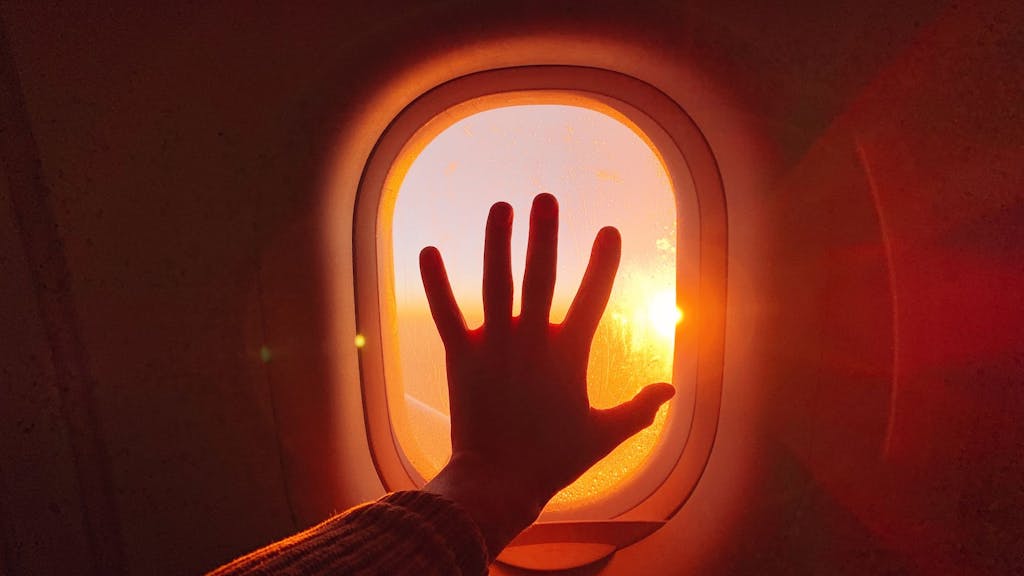 Eine Hand berührt ein Fenster im Flugzeug während des Sonnenuntergangs.
