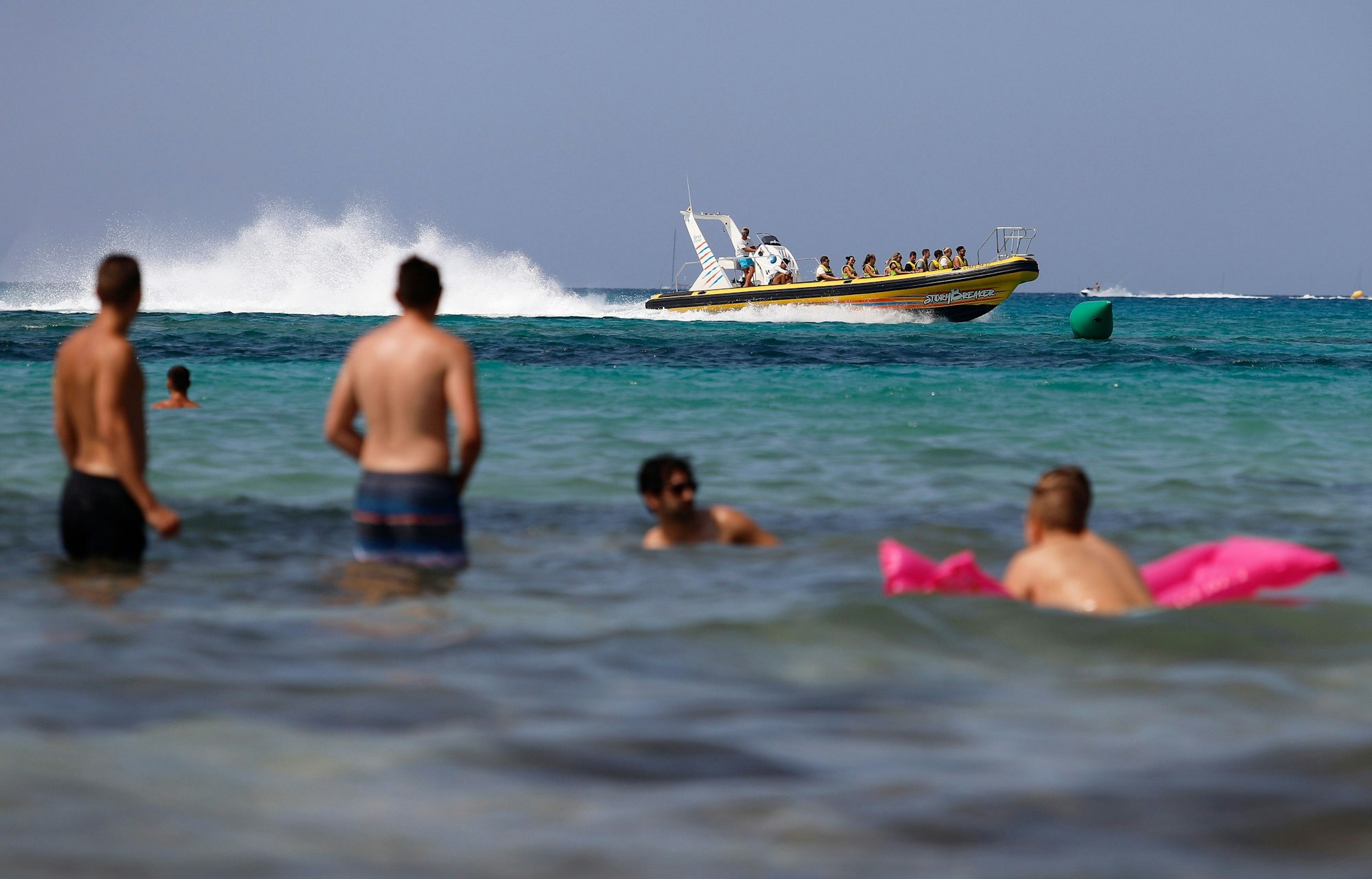 Eine Boot mit Touristen fährt neben den Badegästen am Strand von El Arenal in Palma de Mallorca.
