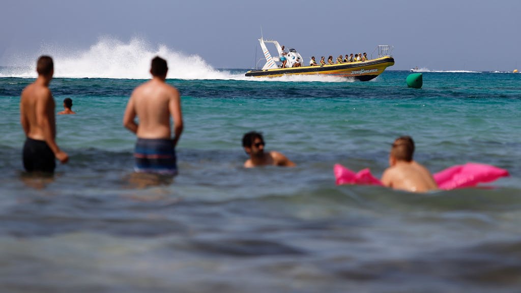Eine Boot mit Touristen fährt neben den Badegästen am Strand von El Arenal in Palma de Mallorca.
