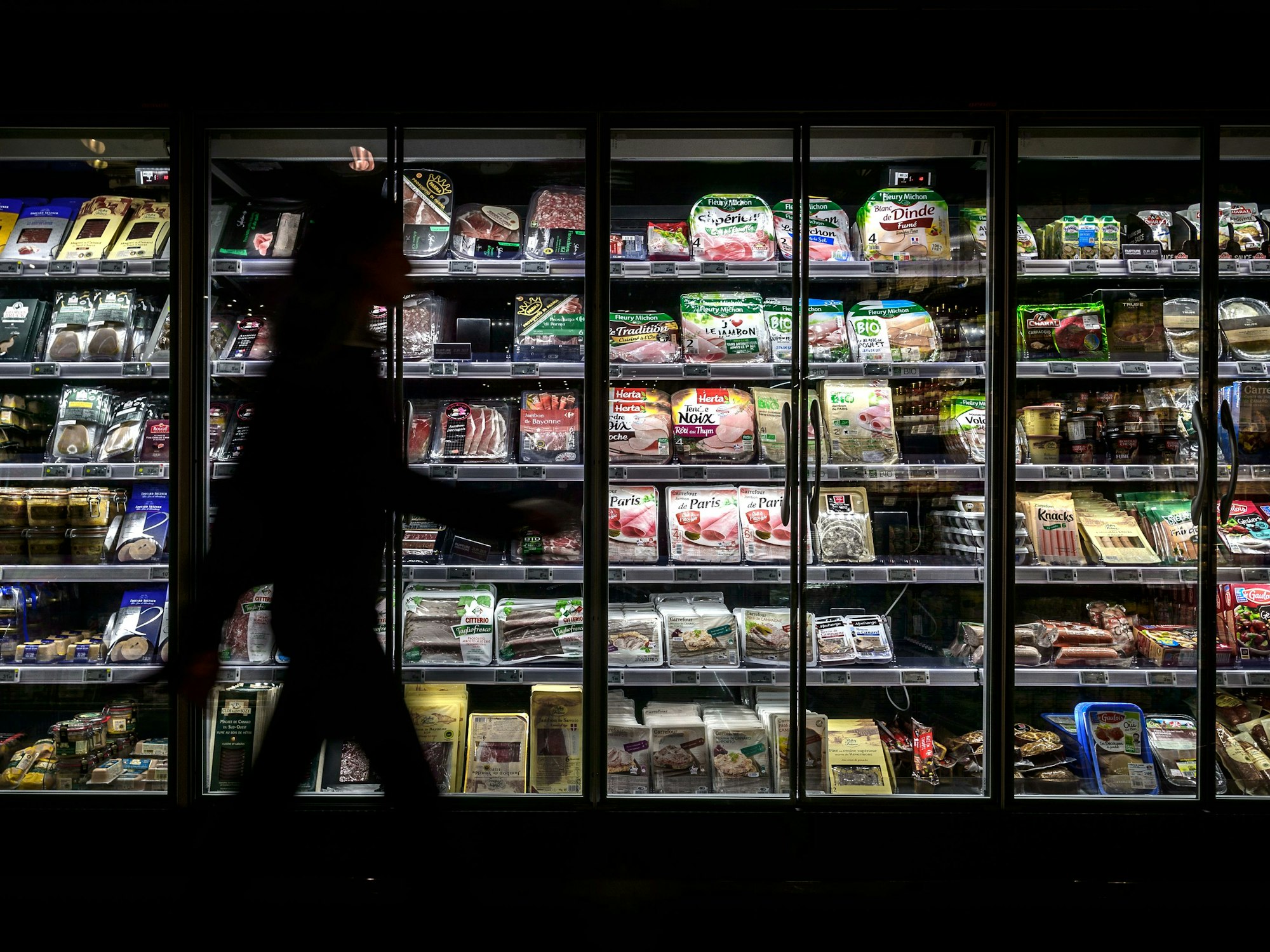 Eine Frau geht an der Kühltheke in einem Supermarkt vorbei.