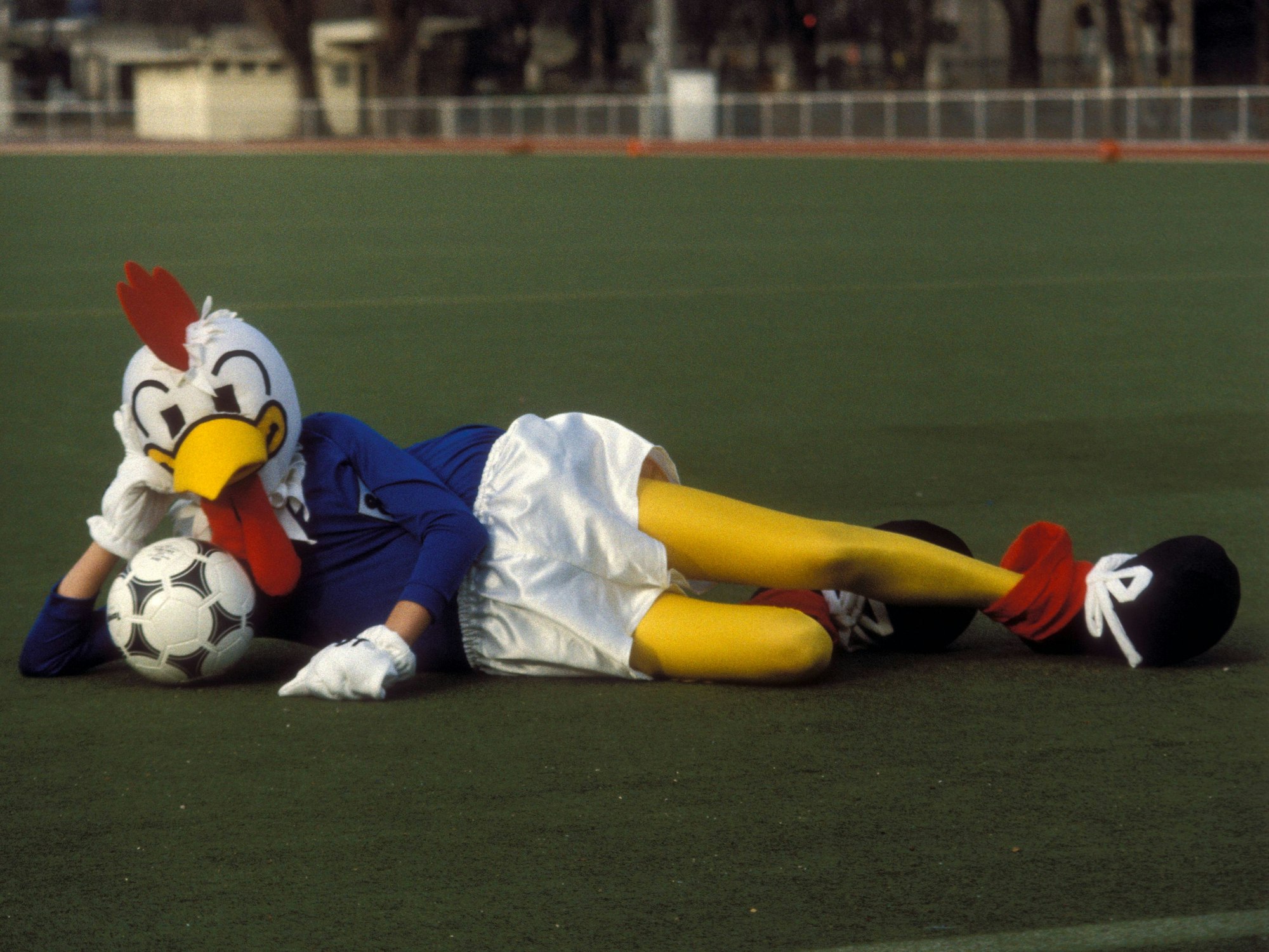 Das Maskottchen „Peno“ für die EURO 1984 liegt mit dem Spielball auf dem Rasen.