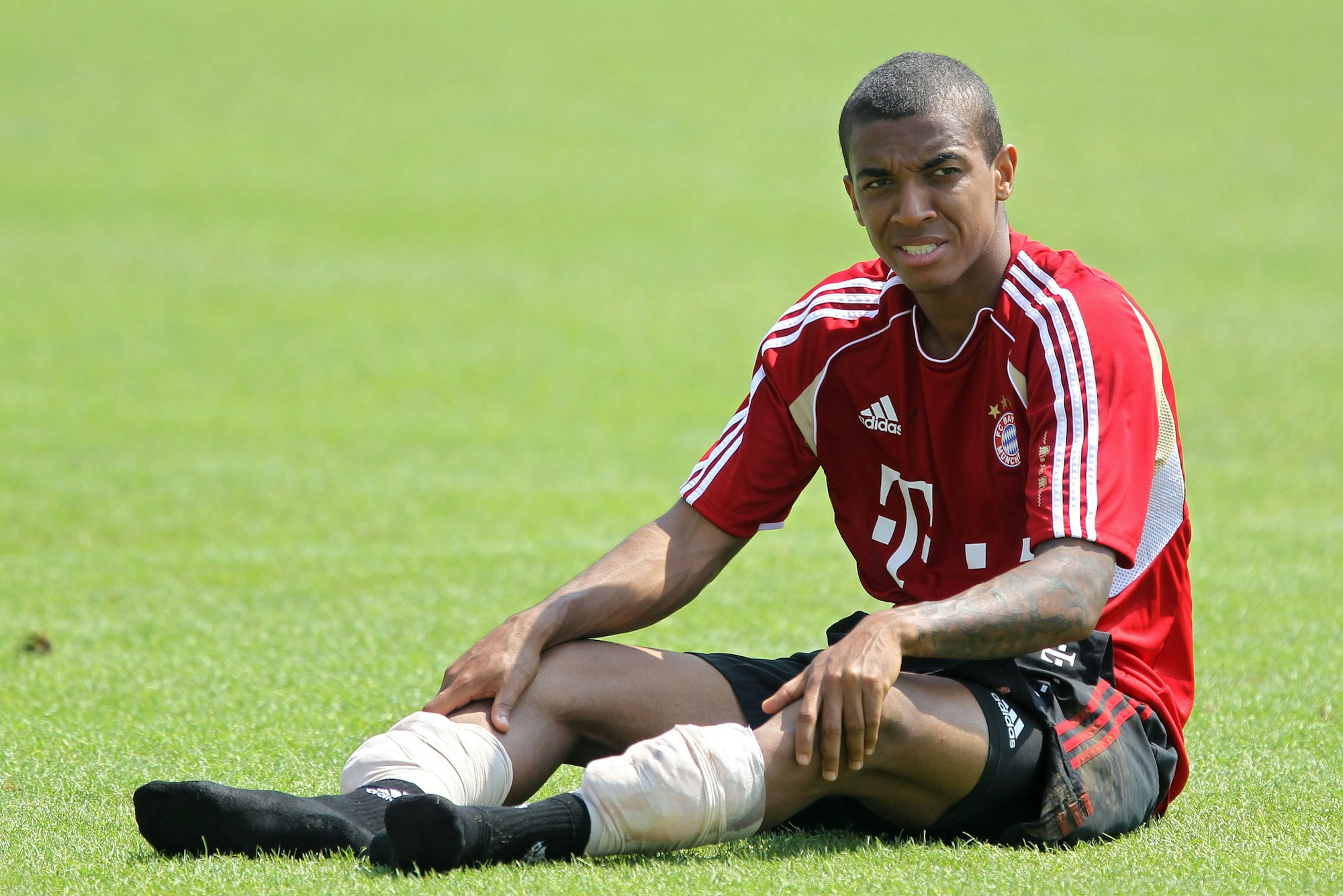 Luiz Gustavo sitzt im Trainingstrikot des FC Bayern München auf dem Rasen.