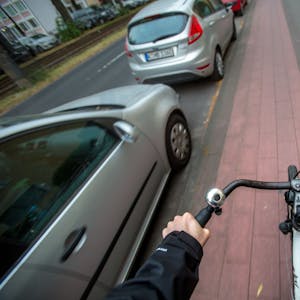 Aus der Perspektive eines Fahrradfahrers ist ein Radweg neben parkenden Autos in Köln zu sehen.