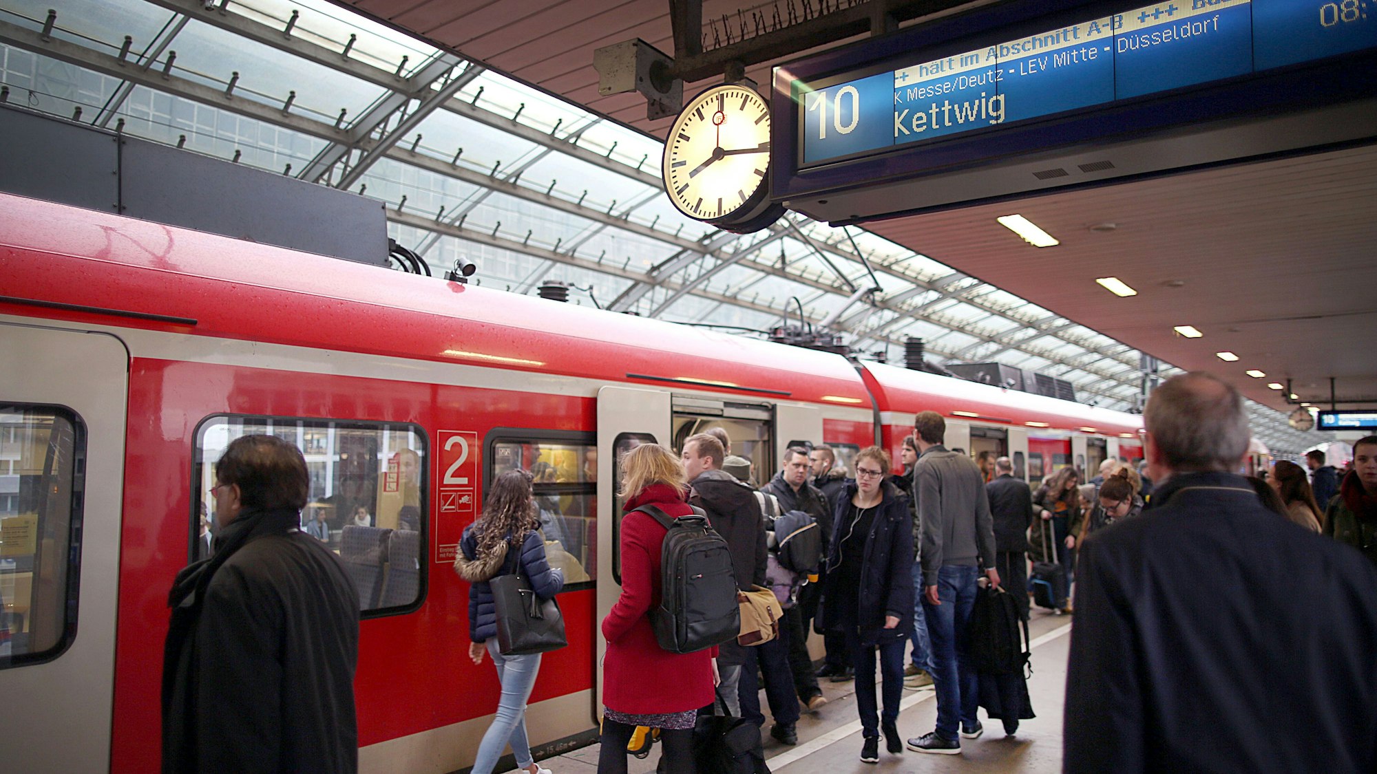 Pendlerinnen und Pendler stehen im Hauptbahnhof Köln vor einer S-Bahn.