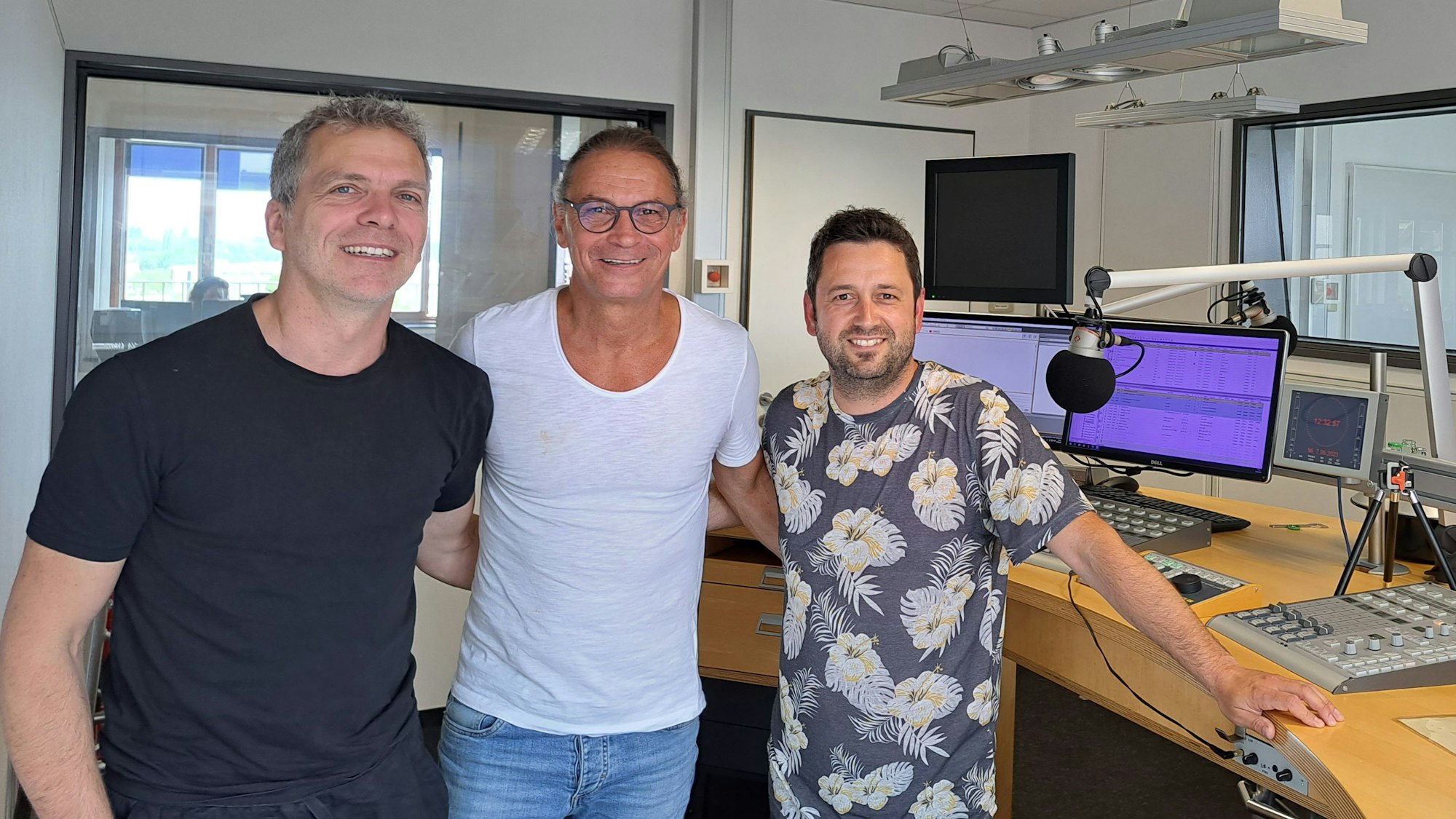 Dirk Kaftan, Peter Brings und Gastgeber Dominik Becker bei der Aufnahme des Podcast. Sie nehmen sich in den Arm und grinsen in die Kamera.