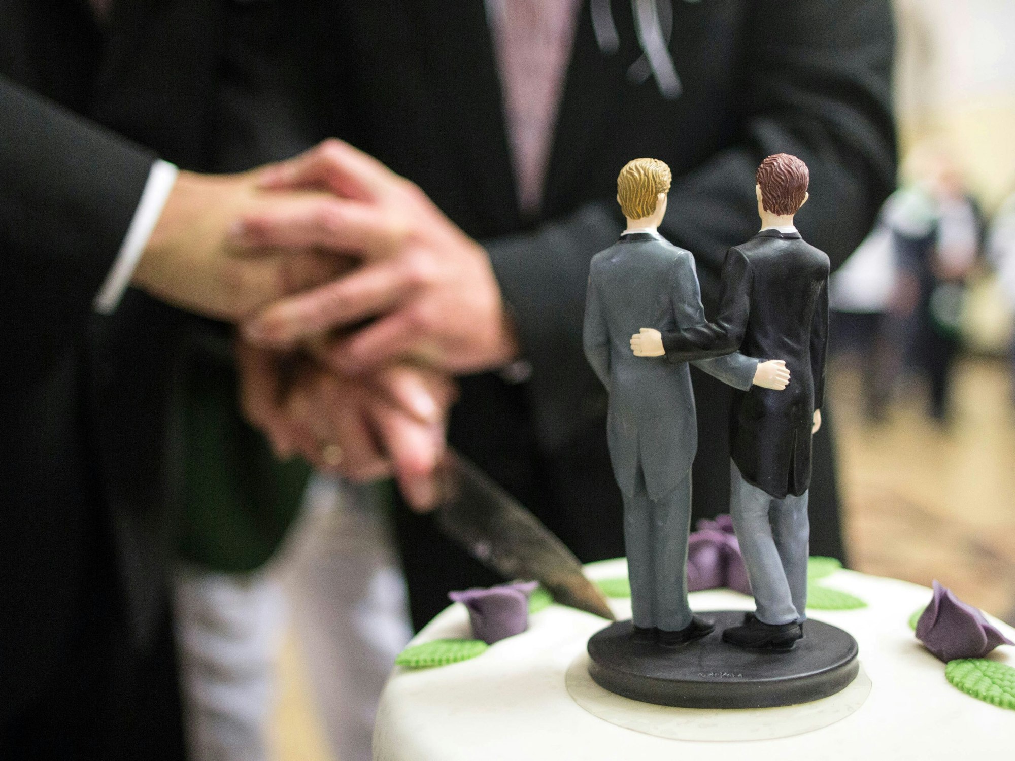 Zwei Männer schneiden nach ihrer Eheschließung im Rathaus eine Hochzeitstorte an.