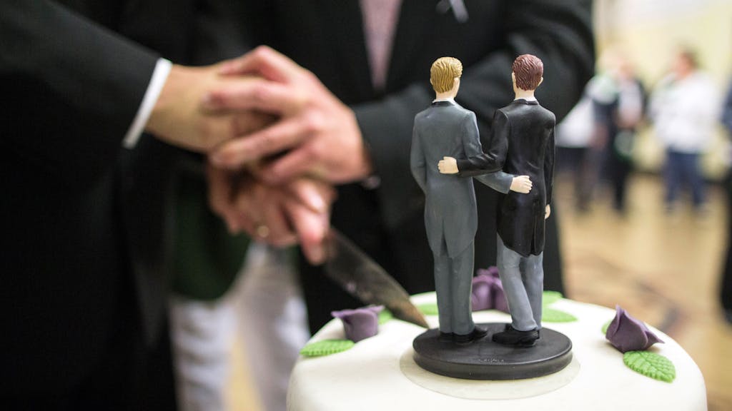 Zwei Männer schneiden nach ihrer Eheschließung im Rathaus eine Hochzeitstorte an.