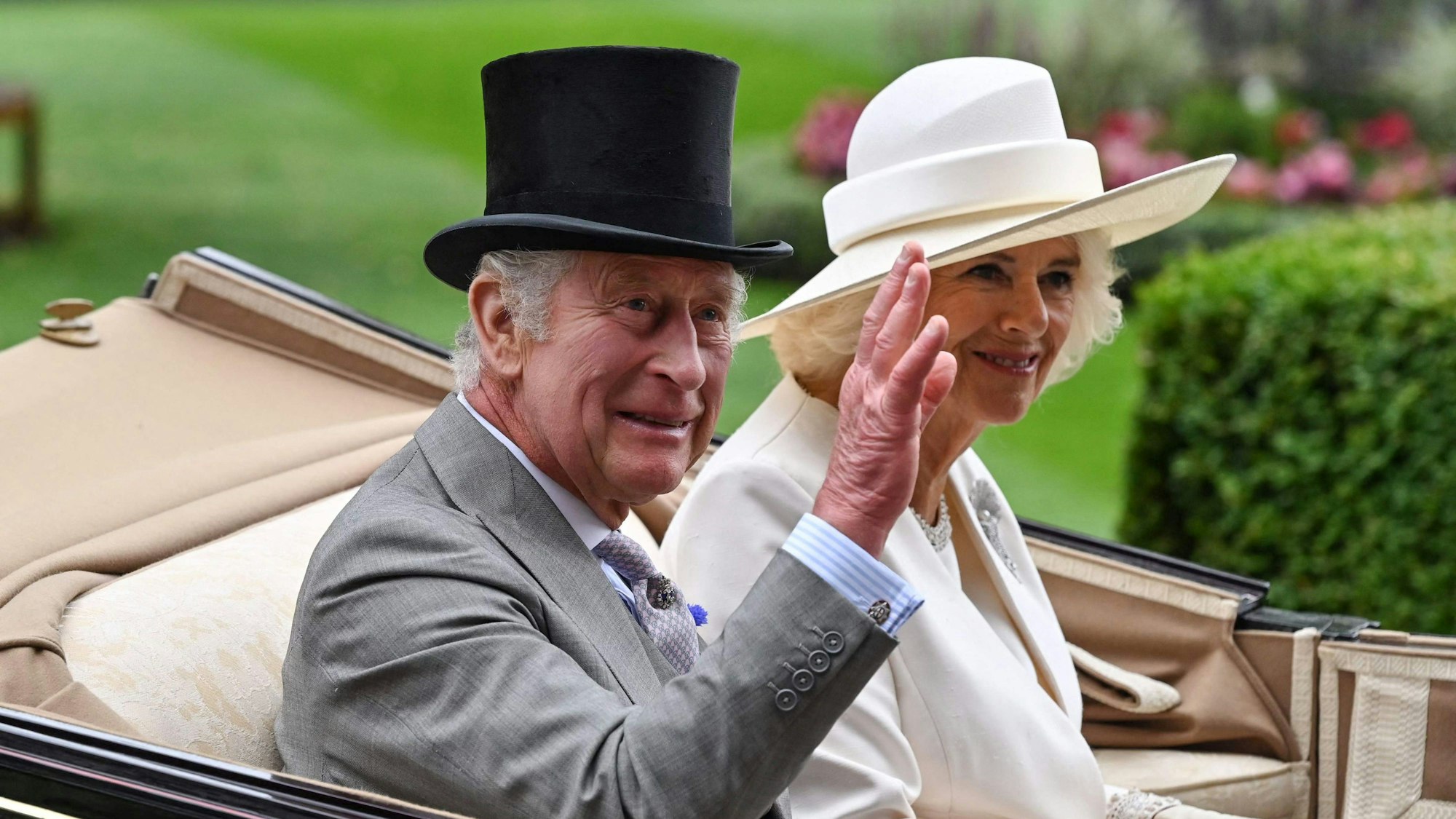 Der britische König Charles III. (l) und Königin Camilla fahren in einer Kutsche vor.