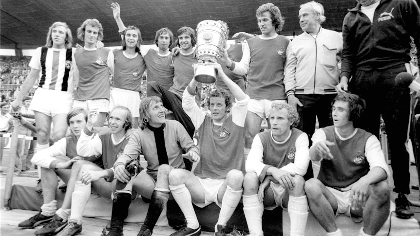 So sehen Pokalhelden und Derbysieger aus! Die Spieler von Borussia Mönchengladbach feiern mit Trainer Hennes Weisweiler 1973 im Düsseldorfer Rheinstadion den Finaltriumph im DFB-Pokal gegen den 1. FC Köln. Herbert Wimmer zeigt dabei stolz die Trophäe.