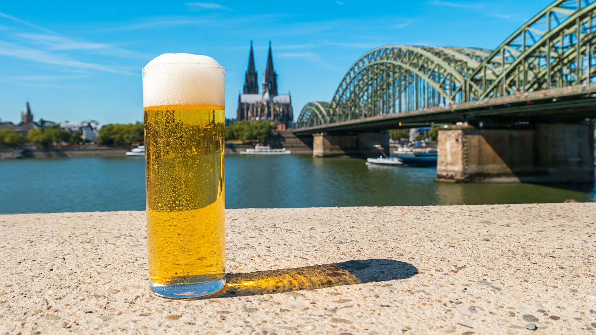 Kölschglas am Rhein. Im Hintergrund die Hohenzollernbrücke und der Dom.