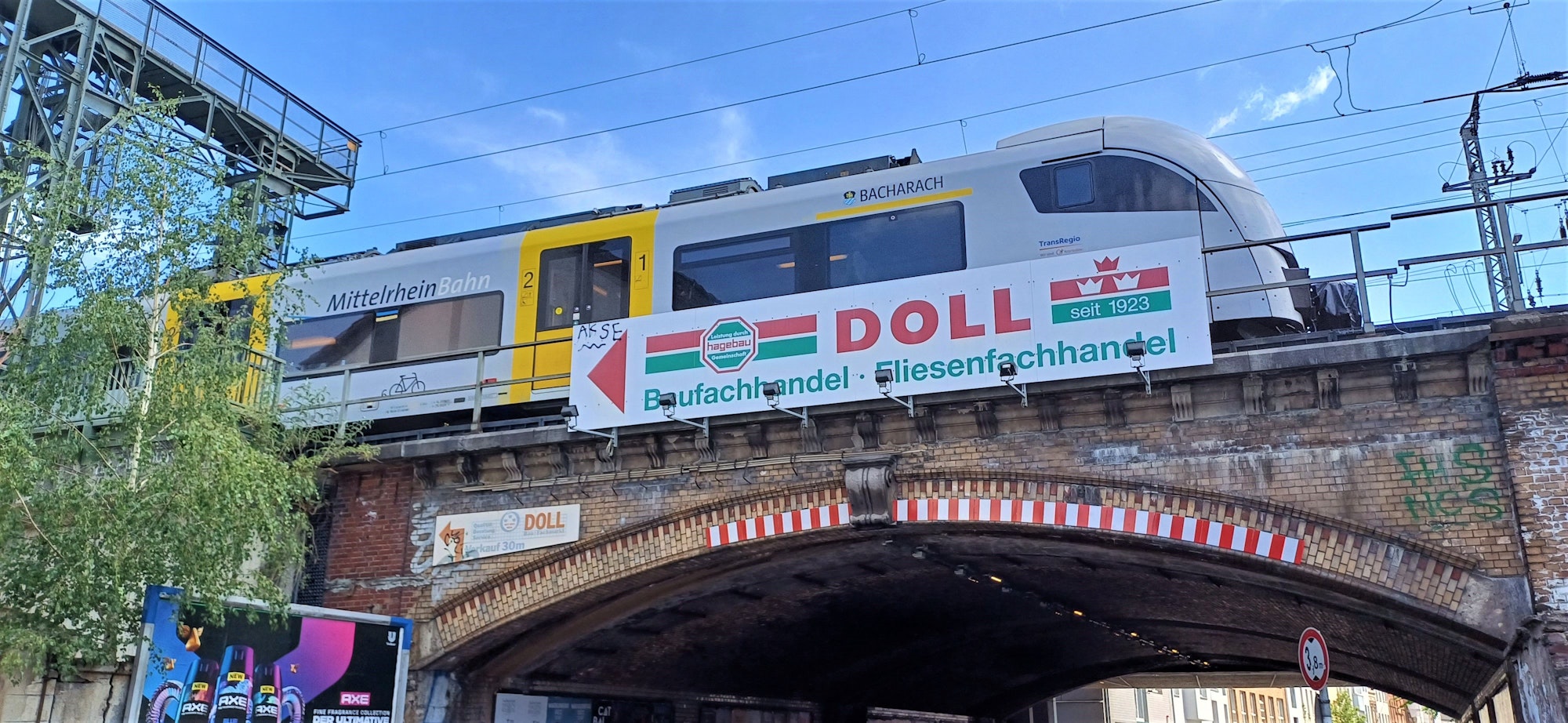 Ein Zug fährt über eine Unterführung mit einem Werbeschild der Firma Doll
