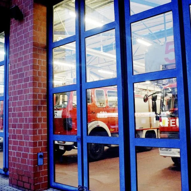 Auf dem Foto sind hinter den geschlossenen Glastüren der Feuerwehrwache Erftstadt die Rettungswagen zu sehen.