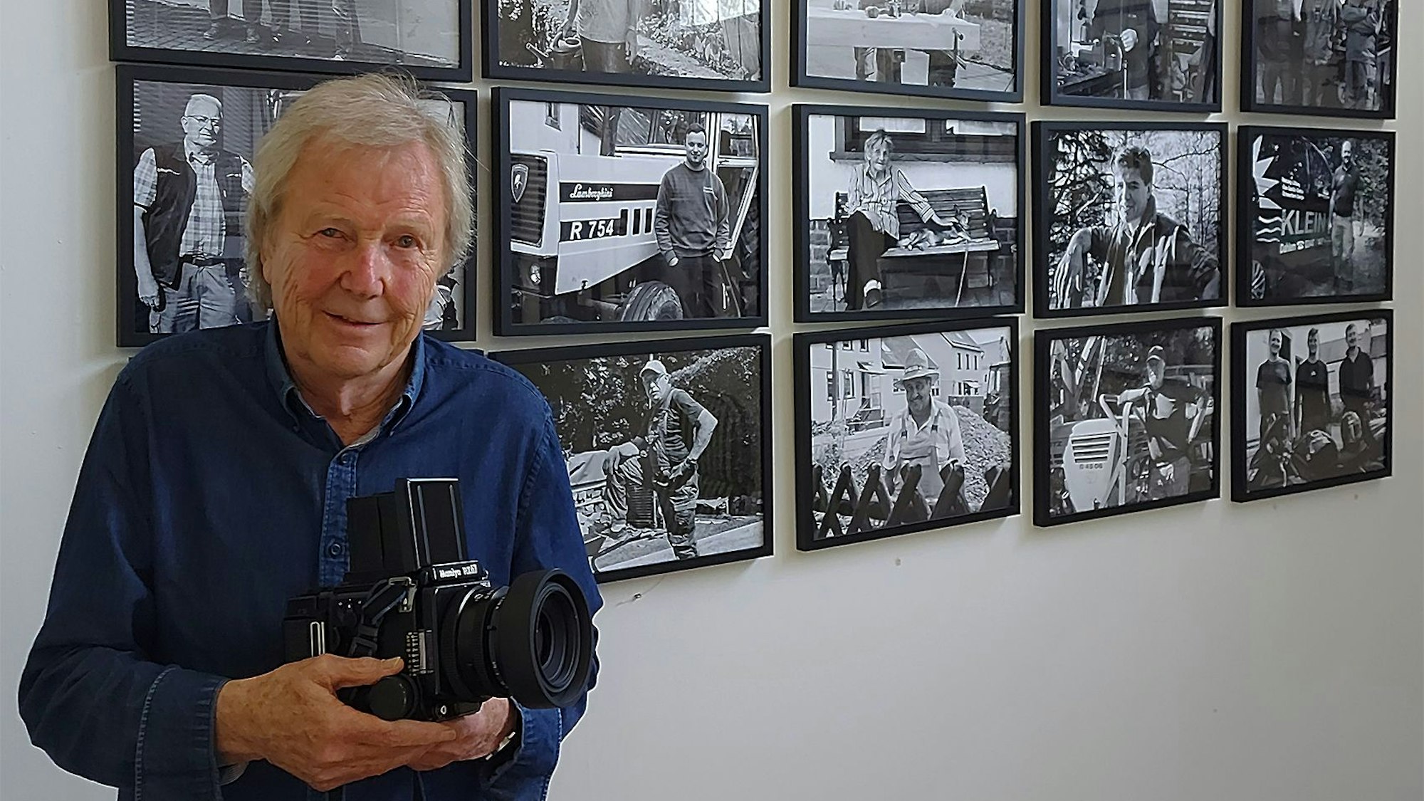 Der Fotograf Dietrich Schubert steht mit seiner Kamara vor einigen seiner Fotos.