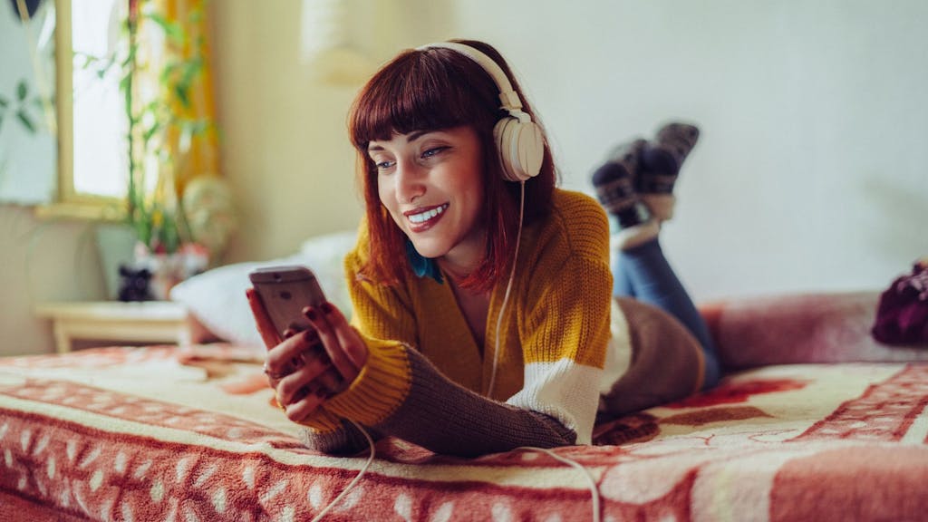 Junge Frau liegt auf Bett mit Kopfhörern und hört Hörbuch