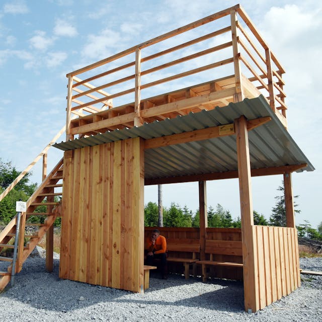 Das Bild zeigt eine Holzhütte, deren Flachdach über eine Treppe bestiegen werden kann.