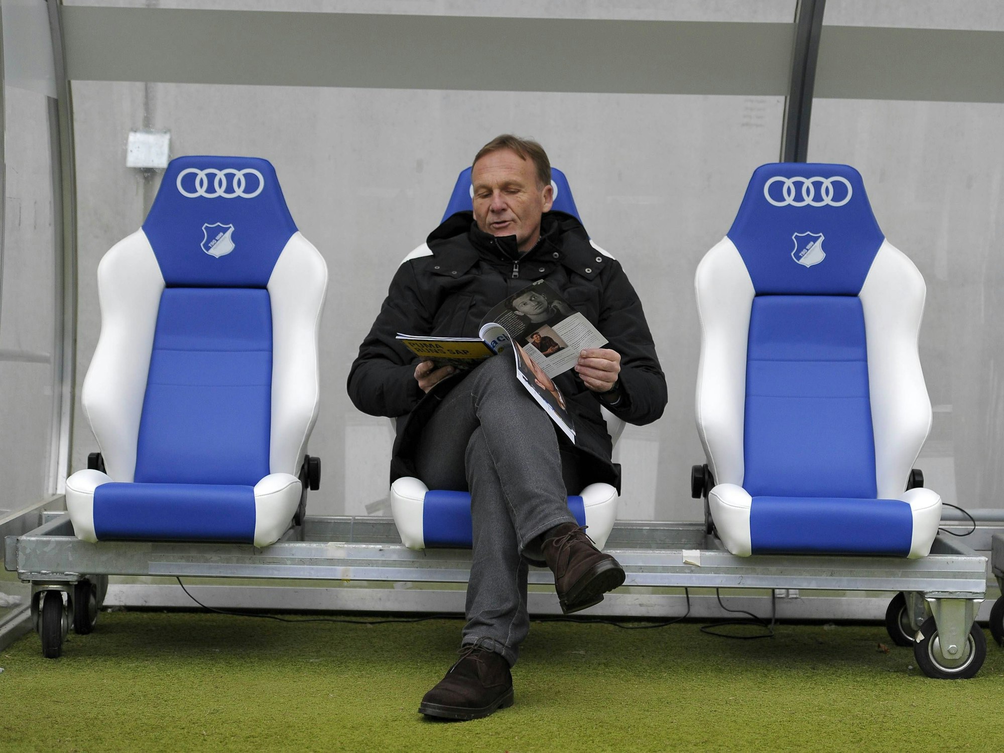 BVB-Geschäftsführer Hans-Joachim Watzke sitzt vor dem Spiel gegen die TSG Hoffenheim im Stadion auf der Auswechselbank und liest die Stadionzeitung.