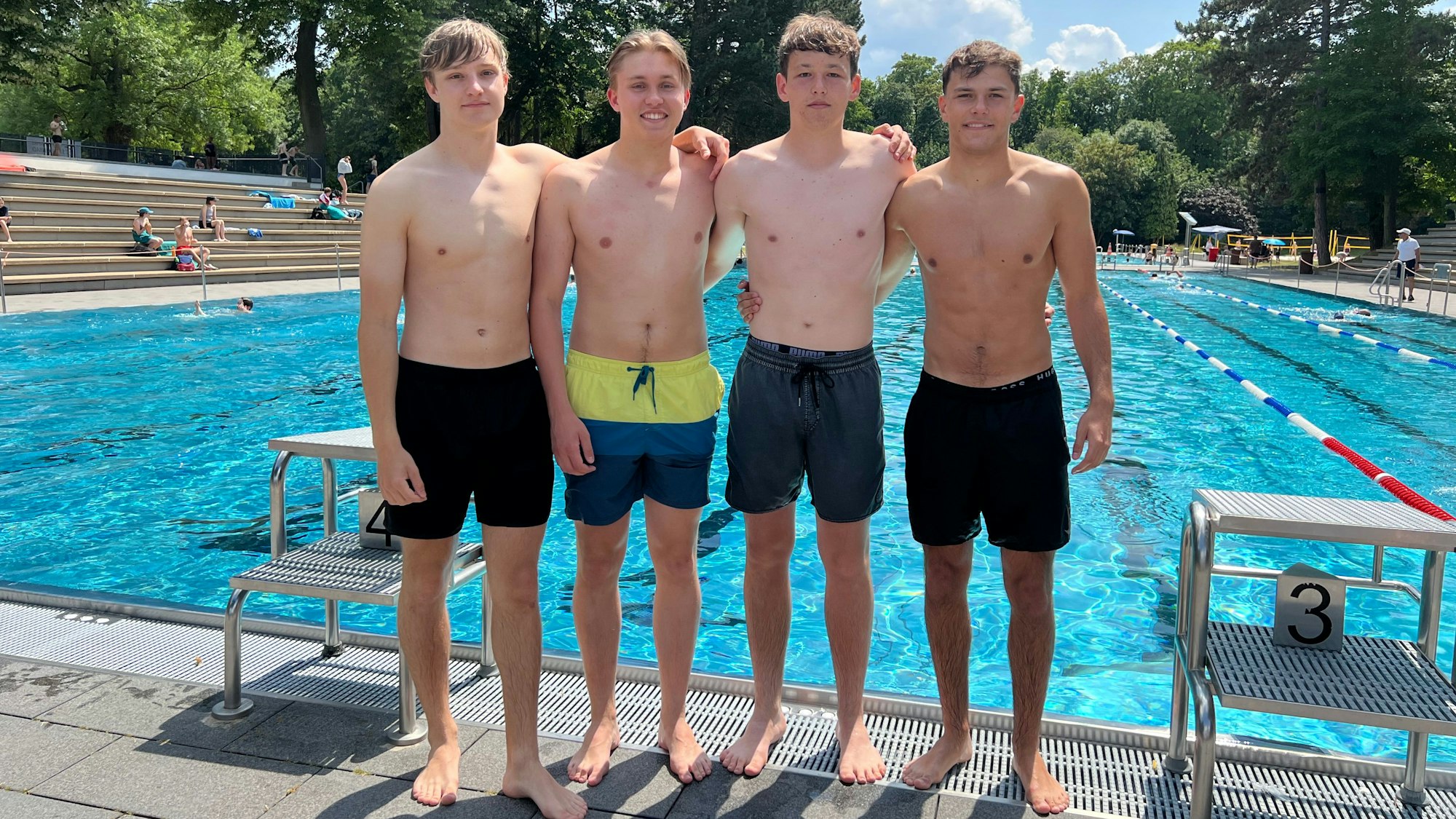 Vier Jungs stehen in Badehose vor dem Schwimmerbecken des Stadionbads.
