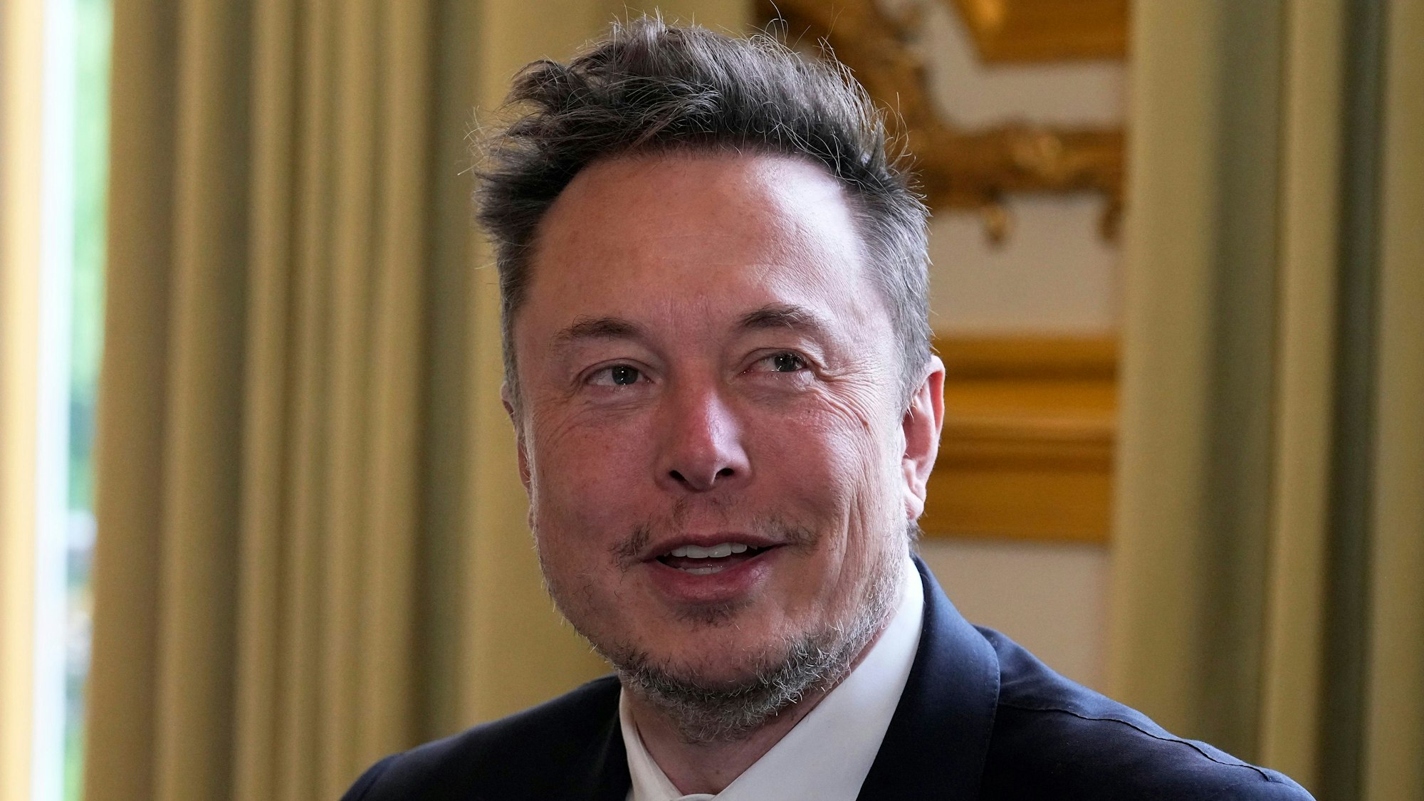 Es ist Elon Musk zu sehen, der leicht lächelnd an der Kamera vorbeischaut.
