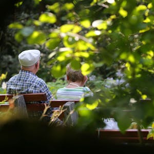 Ein älteres Paar sitzt im Kurpark auf einer Bank im Sonnenschein.