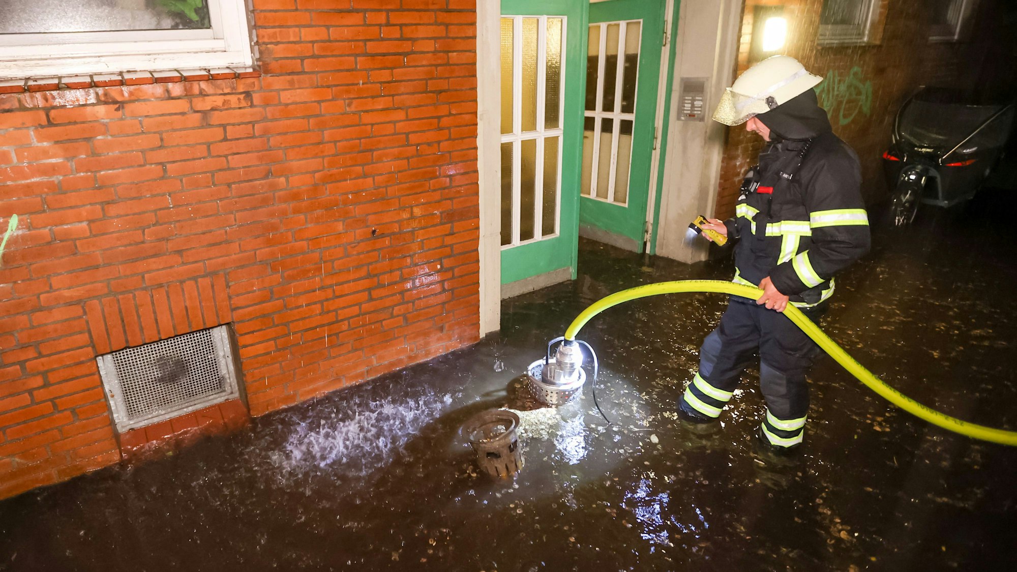 Einsatzkräfte der Feuerwehr pumpen in der Nacht in Hamburg Regenwasser aus einem Keller auf die Straße.