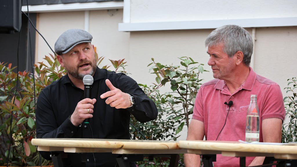 Steffen Baumgart sitzt mit Mikrofon neben Friedhelm Funkel.