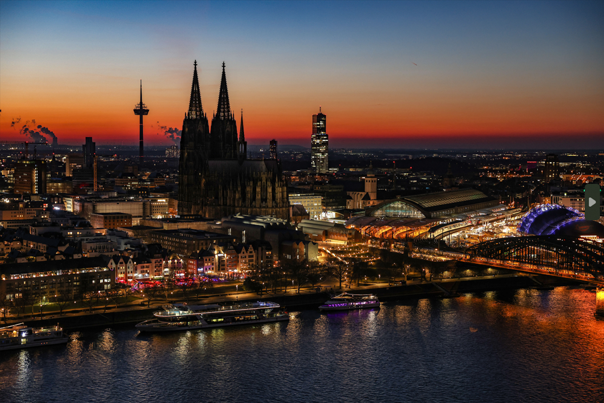 Der Himmel färbt sich hinter dem Rheinpanorama mit Dom und Hauptbahnhof nach dem Sonnenuntergang rötlich.