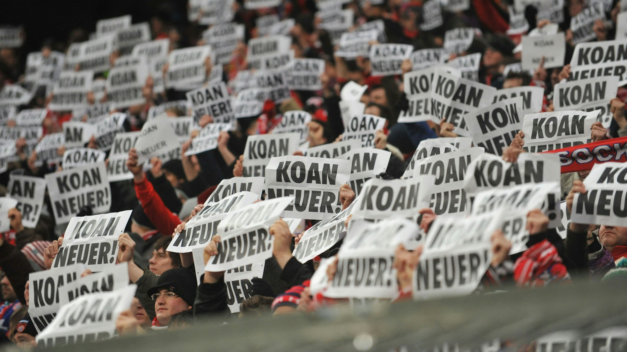 Fans von Bayern München halten Plakate mit der Aufschrift „KOANNEUER!“ hoch.