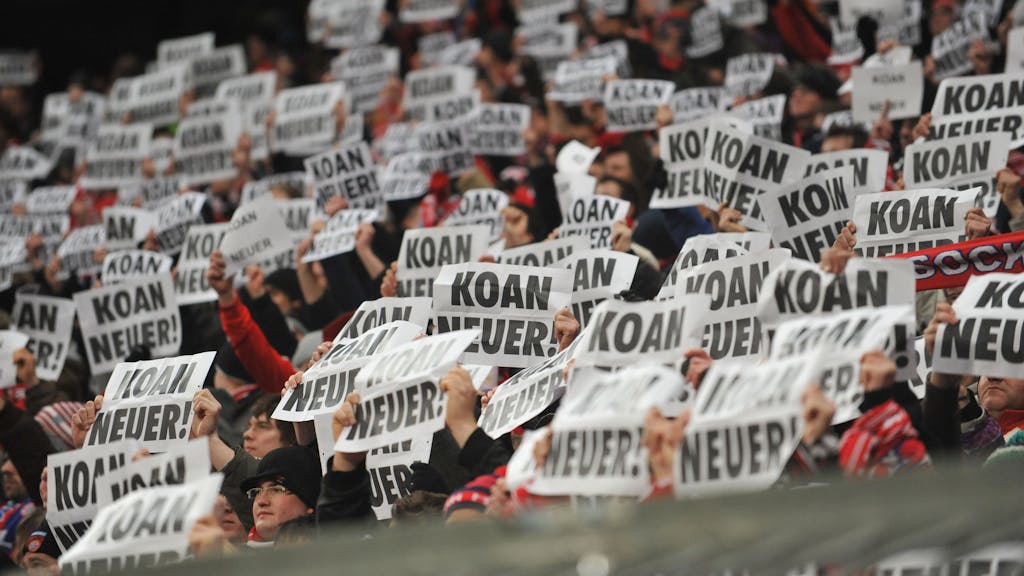 Fans von Bayern München halten Plakate mit der Aufschrift „KOAN&nbsp;NEUER!“ hoch.