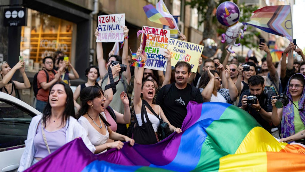 Menschen protestieren mit Schildern und einer großen Regenbogenflagge gegen die LGBTQ-feindliche Politik in der Türkei.