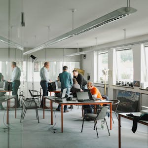 Wirtschaftsnacht Rheinland: Menschen arbeiten in einem minimalistischen Büro mit mehreren Arbeitsplätzen an zwei großen Tischen.