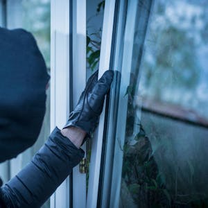 Ein maskierter Einbrecher versucht, ein Fenster&nbsp;zu öffnen.