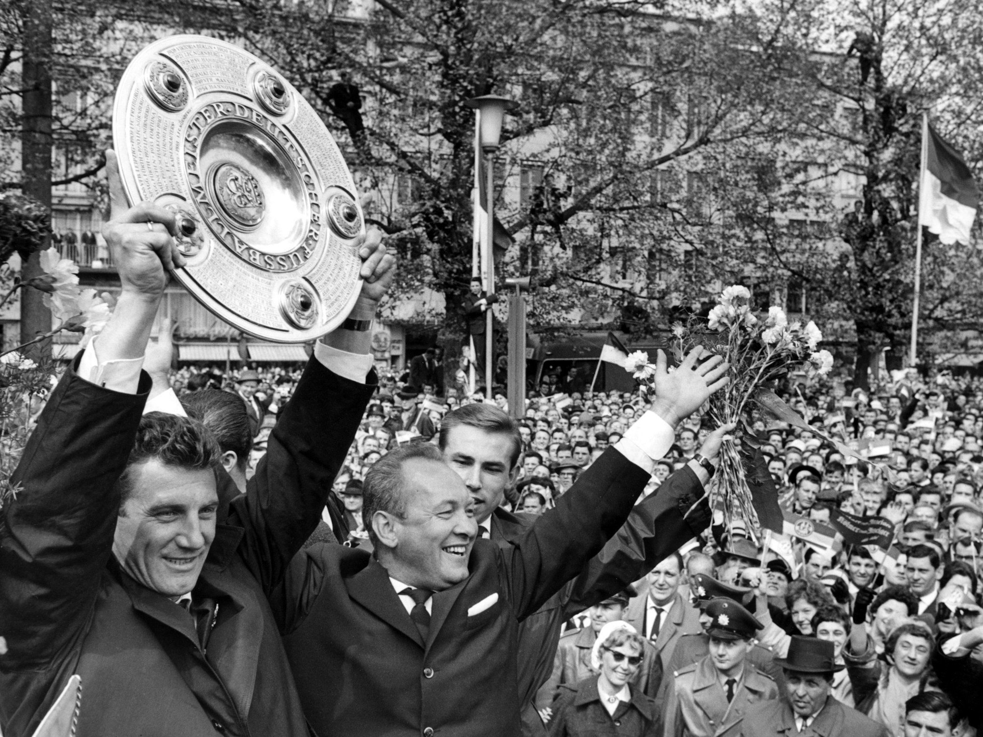 Kapitän Hans Schäfer vom 1. FC Köln (l) jubelt mit der Meisterschale über den Gewinn der Deutschen Fußball-Meisterschaft beim Empfang in der Kölner Innenstadt. 