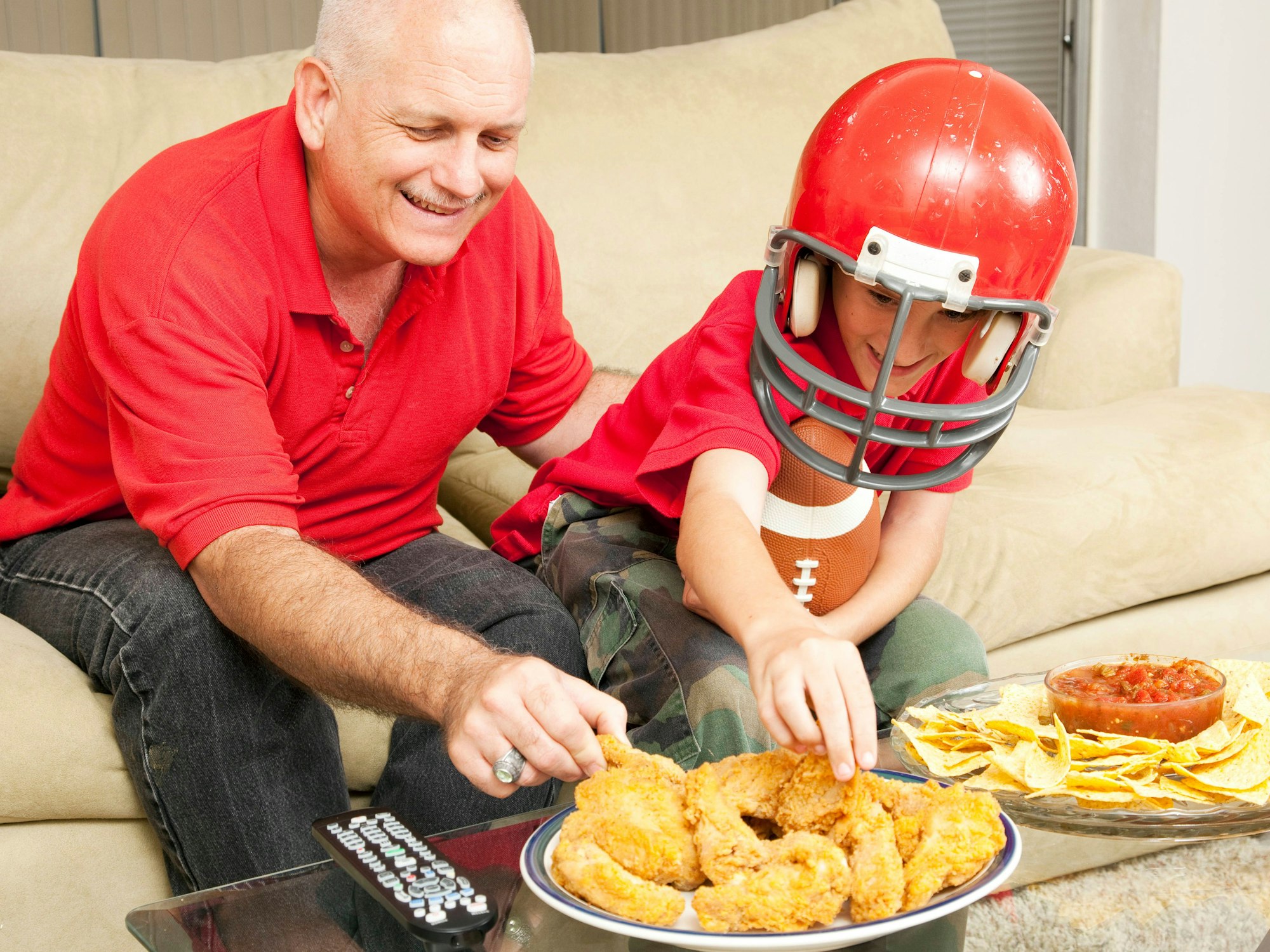 Während ein Vater mit seinem Sohn den Super Bowl schaut, essen die beiden Chicken Wings.