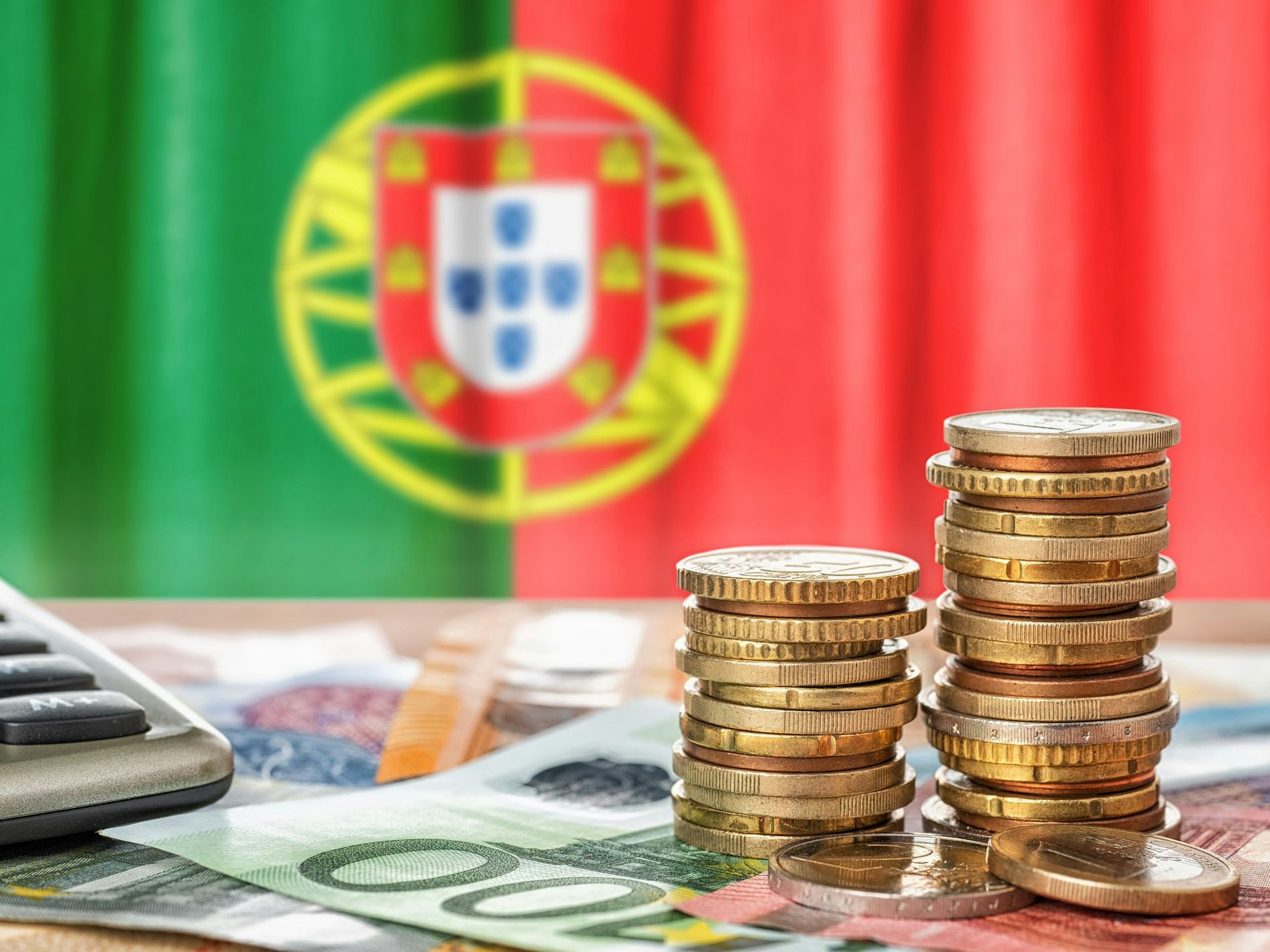 Münzen, Scheine und Taschenrechner vor einer portugiesischen Nationalflagge.