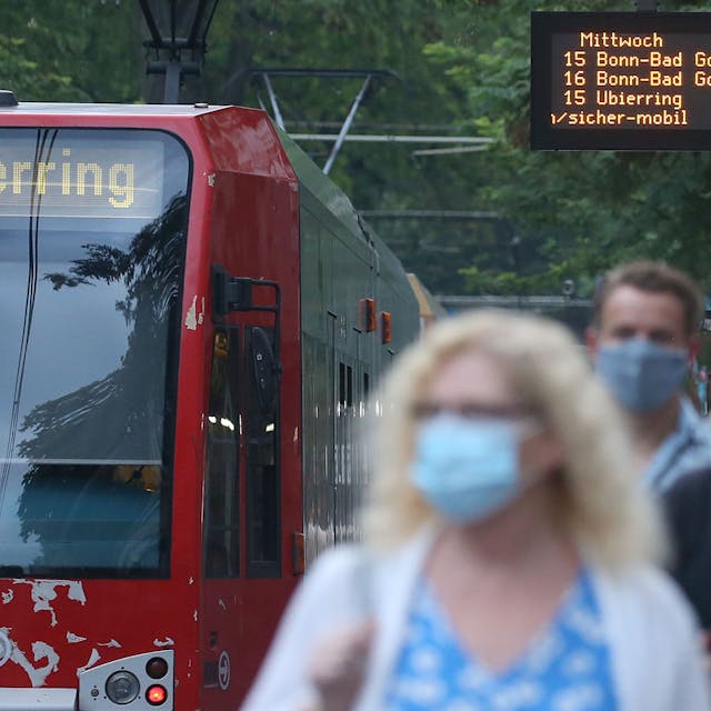 Fahrgäste verlassen einen Bahnsteig neben einer Straßenbahn. Sie tragen Masken.