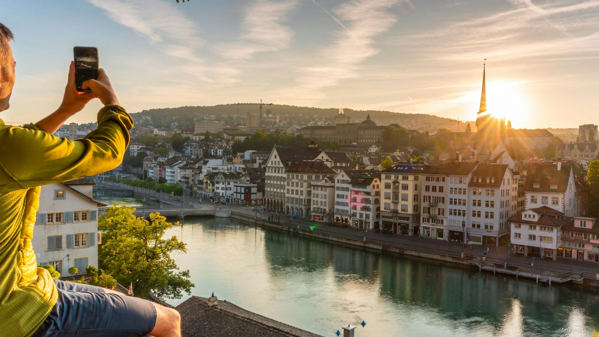 Mann fotografiert mit seinem Smartphone den Sonnenaufgang in Zürich.
