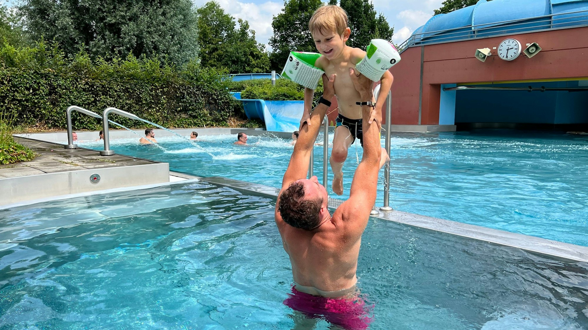 Ein Vater hebt seinen Sohn im Schwimmbecken über seinen Kopf.