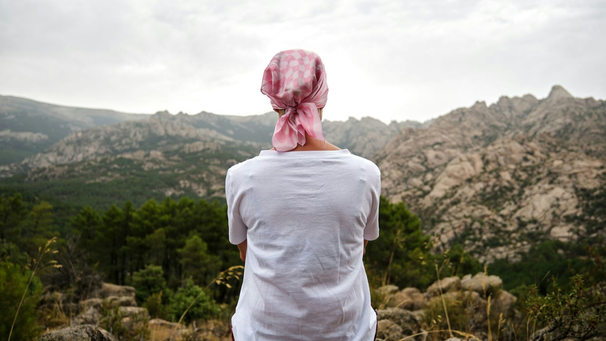 Eine Frau mit Kopftuch sitzt auf einem Berg und schaut in die Landschaft.