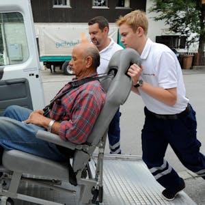 Ein Freiwilligendienstler übt, wie man einen Gehbinderten Menschen in einen Transporter schiebt.